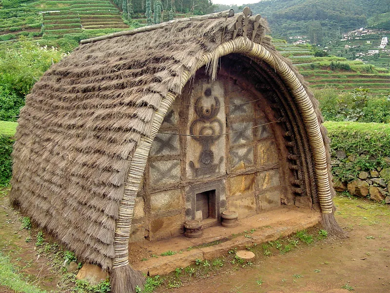 Toda People and Their Traditional Hut in Nilgiris Toda people standing behind a traditional Toda hut in the Nilgiris, showcasing their rich tribal heritage, unique architecture, and cultural legacy.